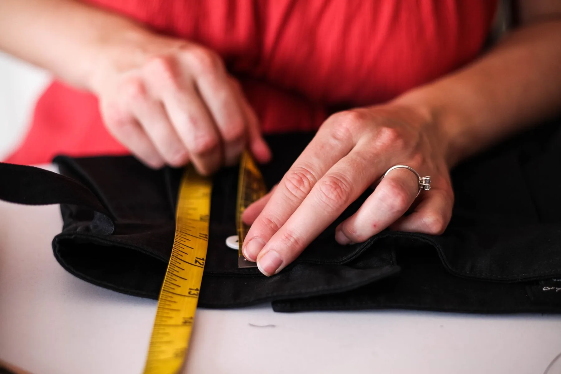 Dressmaker measuring a black garment with a yellow tape measure